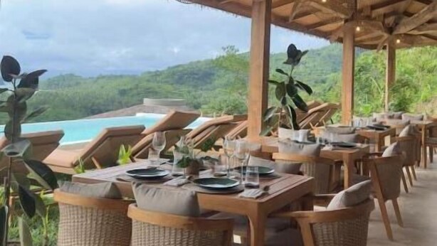 Un espace extérieur abrité, aménagé pour les repas, avec des chaises et des tables en osier, offrant une vue sur une piscine et une végétation luxuriante.