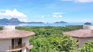 Une vue côtière avec des bâtiments aux toits de chaume, une végétation luxuriante et des îles lointaines.