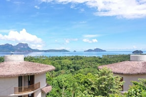 A coastal view with thatched-roof buildings, lush greenery, and distant islands.
