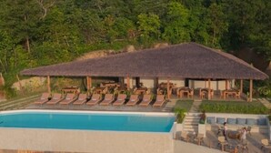 Un espace aménagé au bord de la piscine, avec des chaises longues et un bâtiment dont le toit est recouvert de chaume.