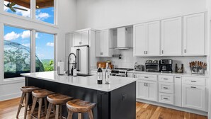 A modern kitchen with white cabinets, a large island with stools, a refrigerator, stove, and various appliances.