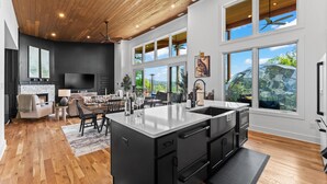 A modern kitchen with a large island, wooden flooring, and large windows offering a view of the outdoors.