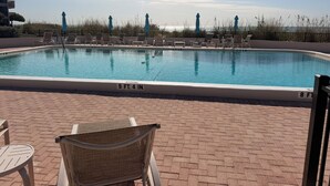 Piscina rectangular con sillones de descanso y sombrillas, rodeada de un patio de ladrillo.