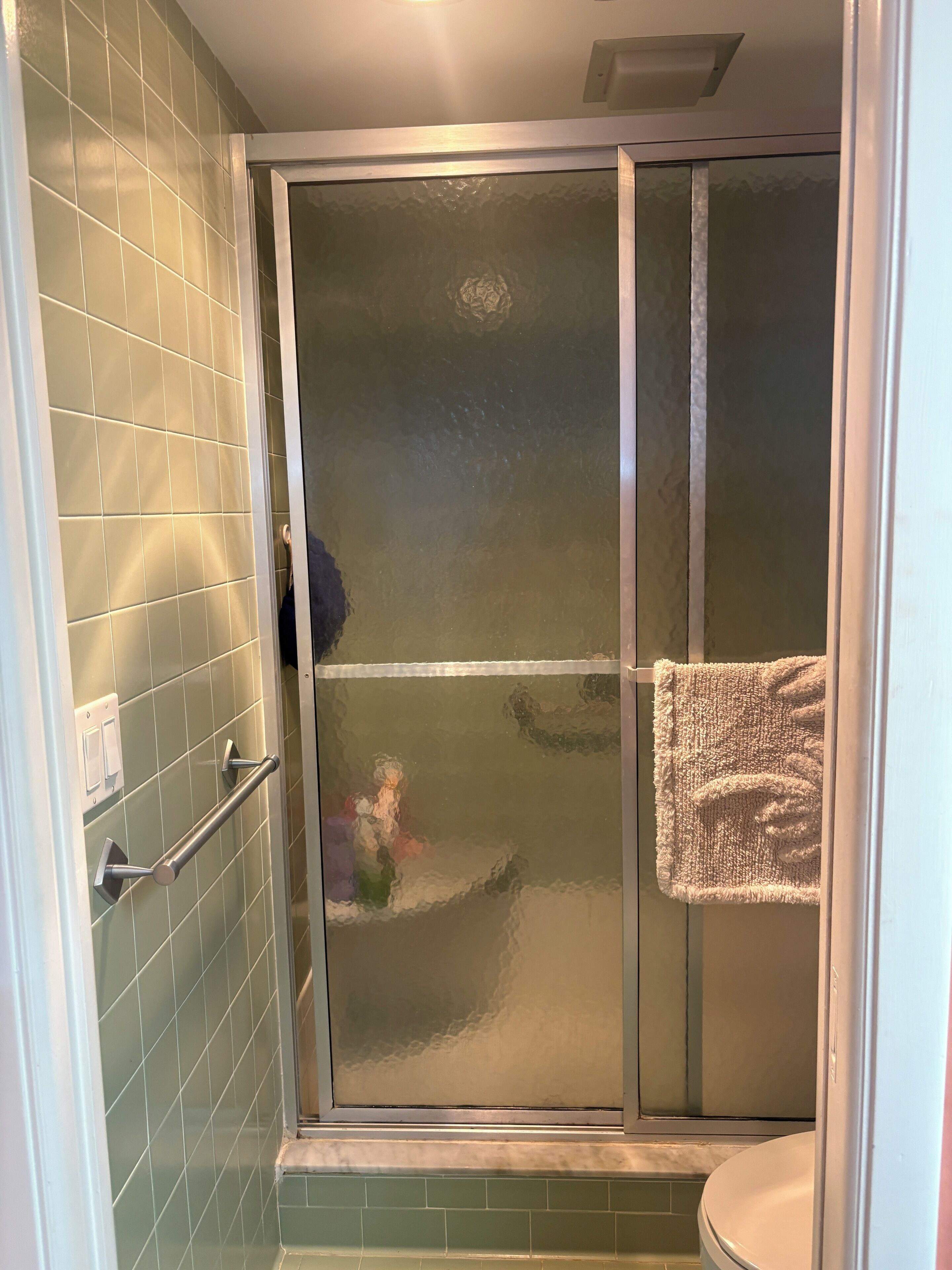 Een badkamer met een douchecabine van glas, een handdoekrek en een toilet.