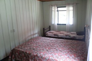 A bedroom with a single bed, a window with curtains, and a wooden headboard. - Casa de Campo com Churrasqueira e Fog o a Lenha (Paranaguá)