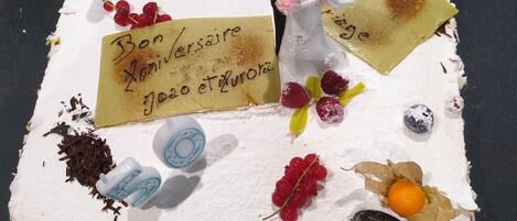 A square cake with various decorations and text, including a couple figurine, red berries, and a handwritten note.