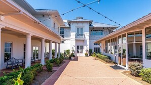 Une cour d’hôtel avec un chemin central, des espaces de repos abrités et un grand bâtiment doté d’un balcon.