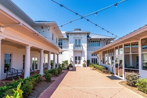 A hotel courtyard with a central pathway, covered seating areas, and a large building with a balcony. - NEW ON RENTAL Beach Club Condo with Gulf Views, Spa & Resort Amenities (Gulf Shores)