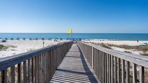 Une promenade en bois menant à une plage agrémentée de parasols et d’un drapeau.