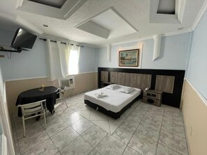 Una habitación de hotel con cama, escritorio, silla, televisión y un cuadro en la pared.