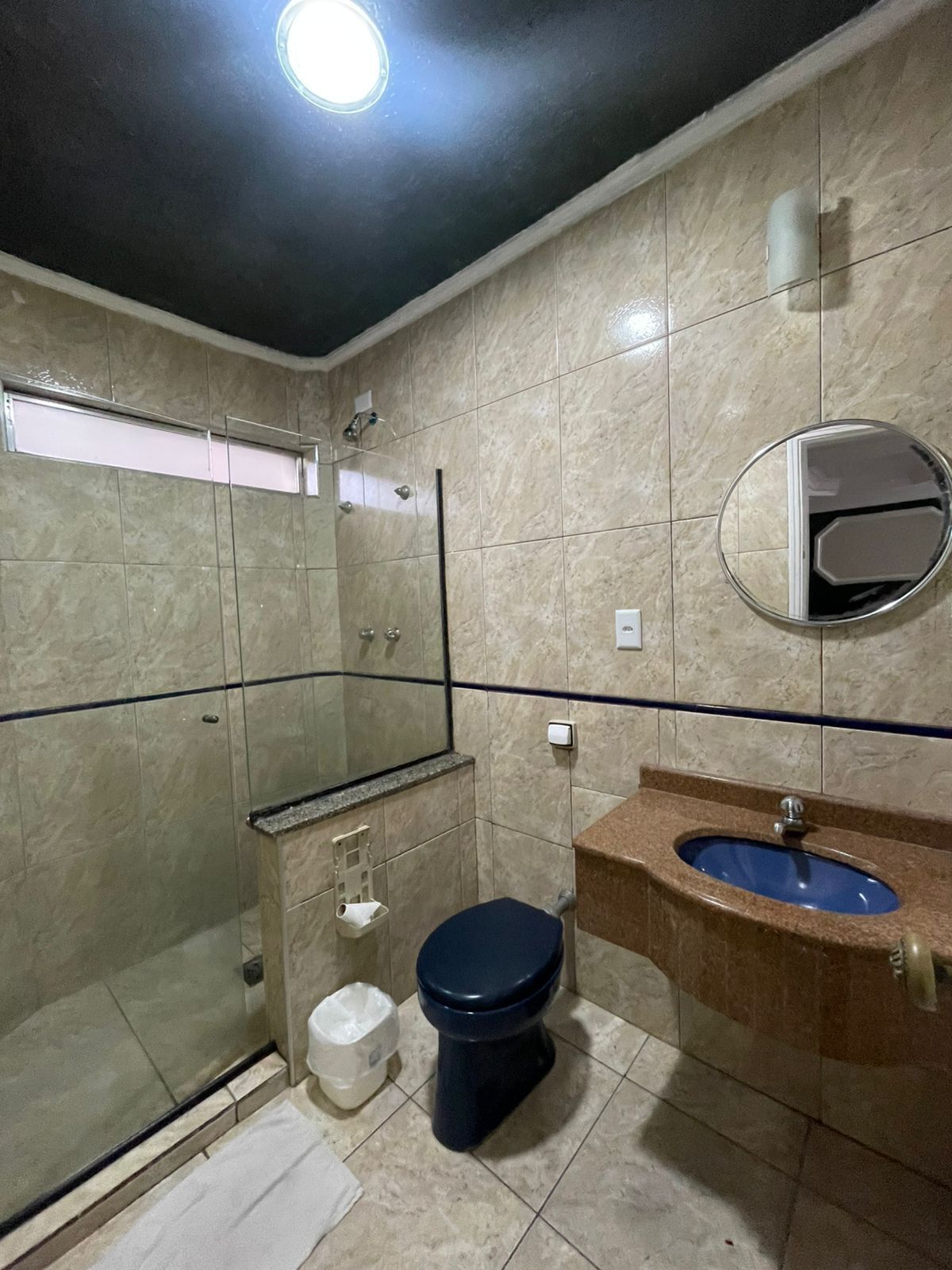 Un bagno con cabina doccia in vetro, un water, un lavandino con lavabo blu e uno specchio.