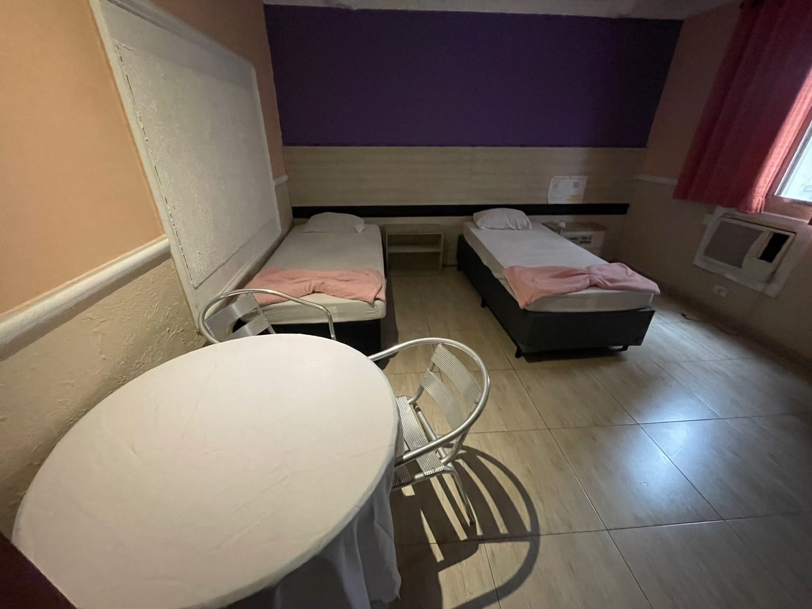 Um quarto pequeno com duas camas de solteiro, uma mesa redonda e uma cadeira.