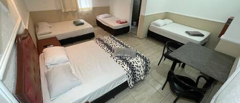 A compact hotel room with two single beds, a small desk, a chair, a TV, and a shower area.