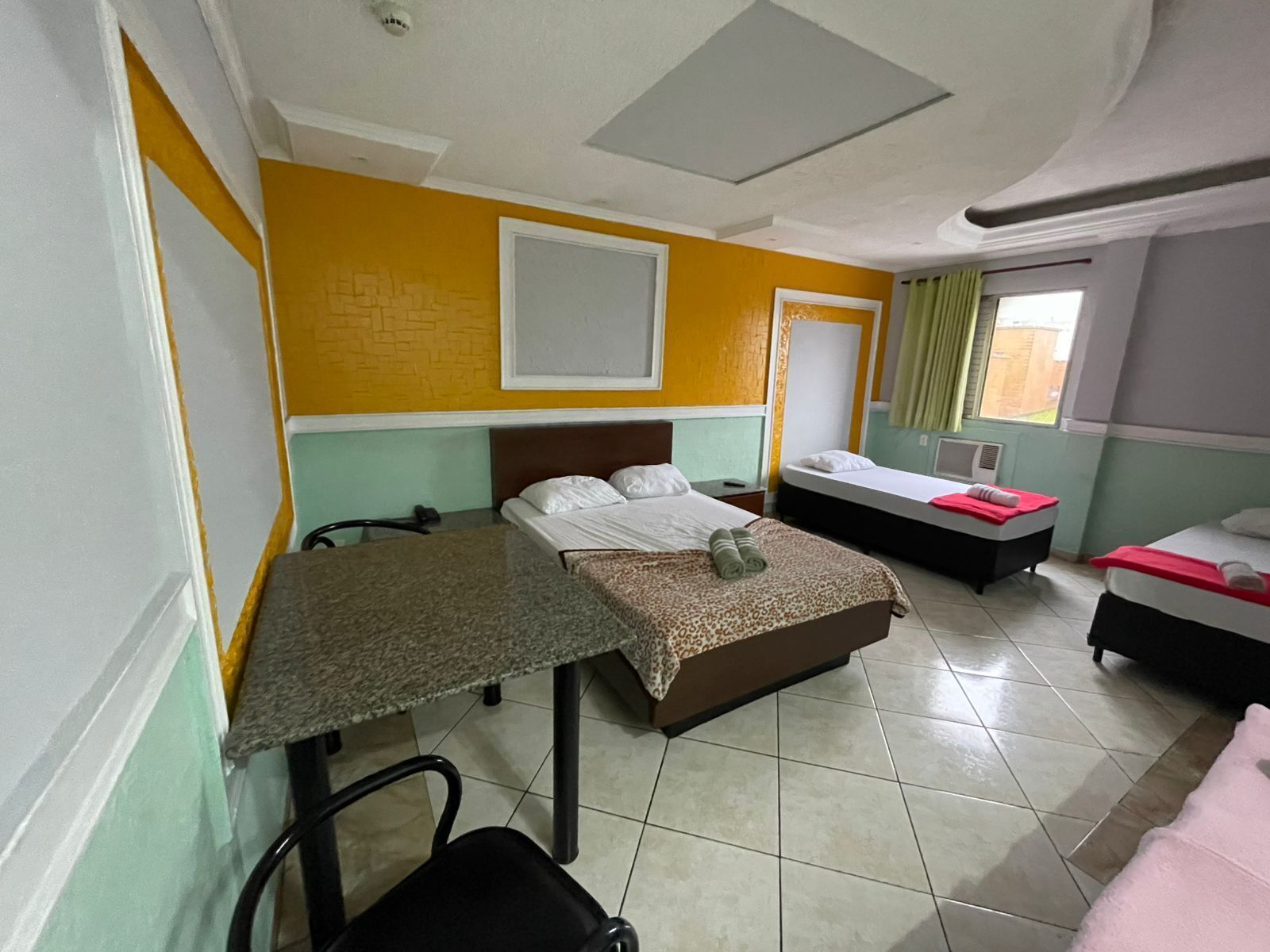 A hotel room with two beds, a table, a chair, and a window with curtains.