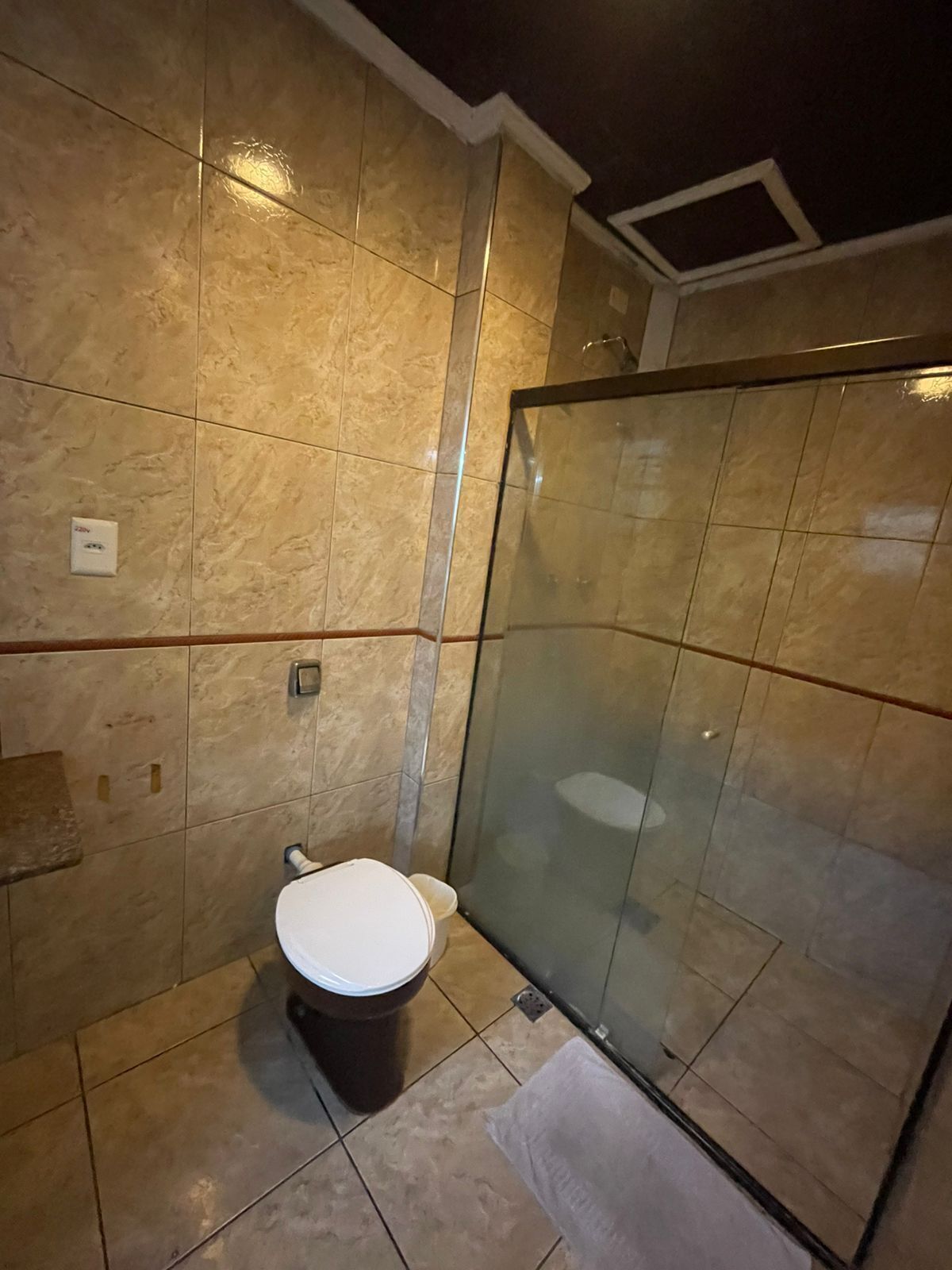 A bathroom with a toilet, a glass shower enclosure, and a tiled floor.