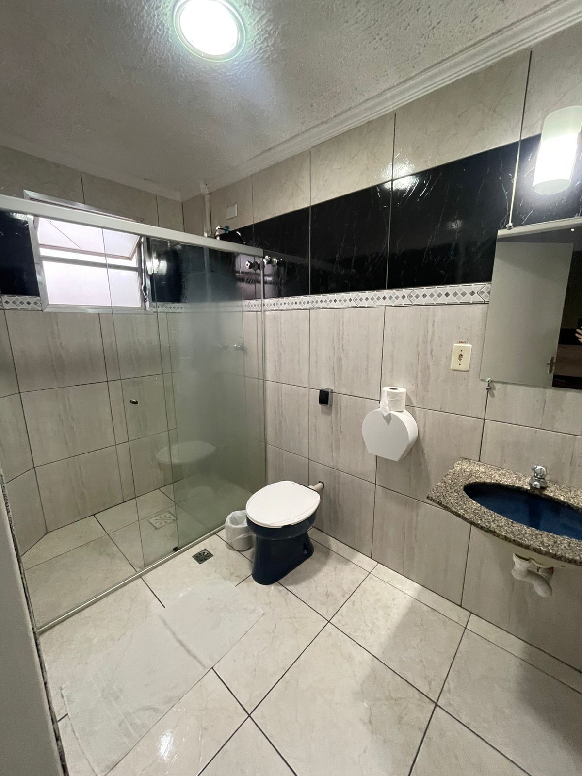Un bagno con il water, una cabina doccia in vetro, un lavandino e un pavimento piastrellato.