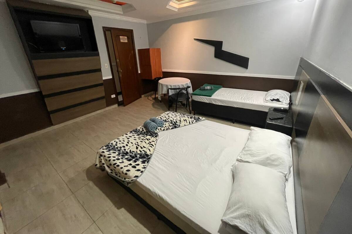 Ένα μικρό και λειτουργικό δωμάτιο ξενοδοχείου με ένα κρεβάτι, ένα μικρό τραπέζι, μια καρέκλα και μια τηλεόραση.