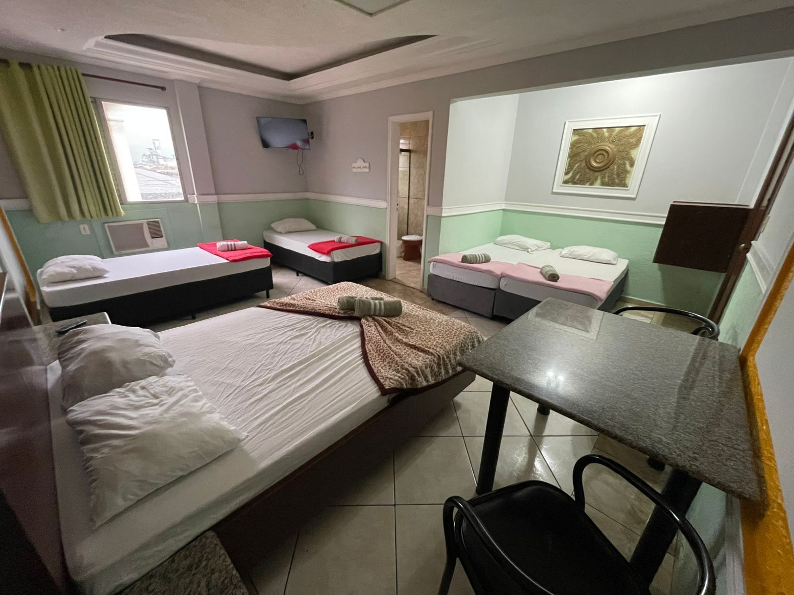 Habitación de hotel con dos camas individuales, una cama doble, una mesita, una silla y un televisor en la pared.