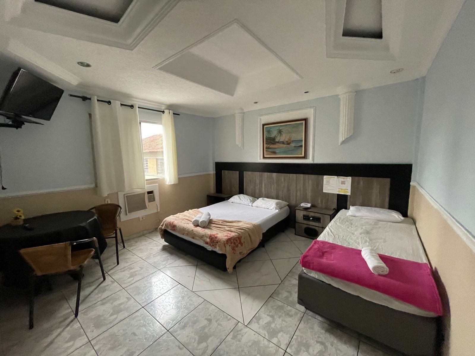 Une chambre d’hôtel avec deux lits, un bureau, une chaise, une télévision et une fenêtre avec des rideaux.