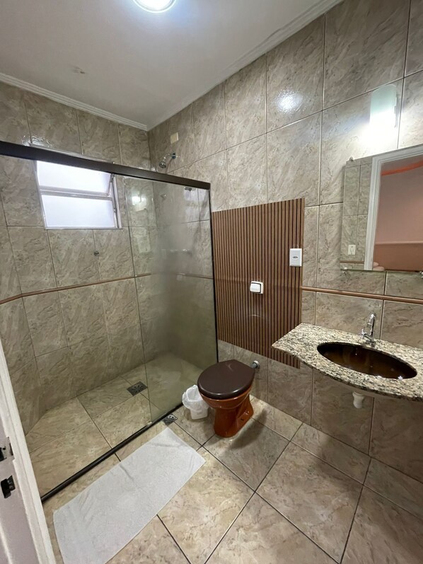 Un baño con ducha de vidrio, inodoro, lavabo con encimera de mármol y espejo sobre el lavabo.