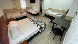Ein Hotelzimmer mit drei Betten, einem Schreibtisch, einem Stuhl, einem Fernseher und einem Vorhangfenster.