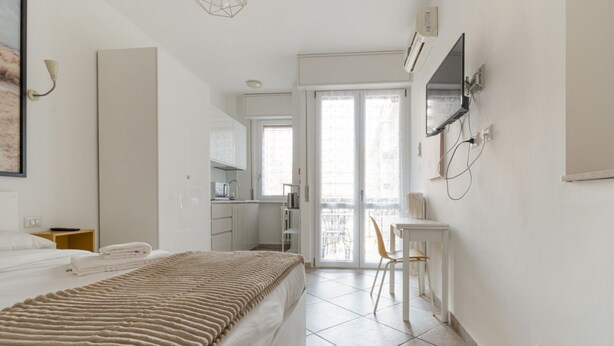 A bedroom with a bed, a desk, a chair, and a view of a balcony. - GuestHost - A comfortable 30 square meters studio, perfect for two people, located on the first floor of a building with an elevator (NOT suitable for people with reduced mobility).The apartment is just steps from Pasteur metro station and within a 10-mi (Milan)
