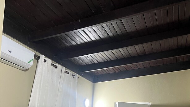 Ein Einzelbett mit weißer Bettdecke und Kissen, eine Fernbedienung auf dem Bett, eine weiße Tür und ein Deckenventilator.