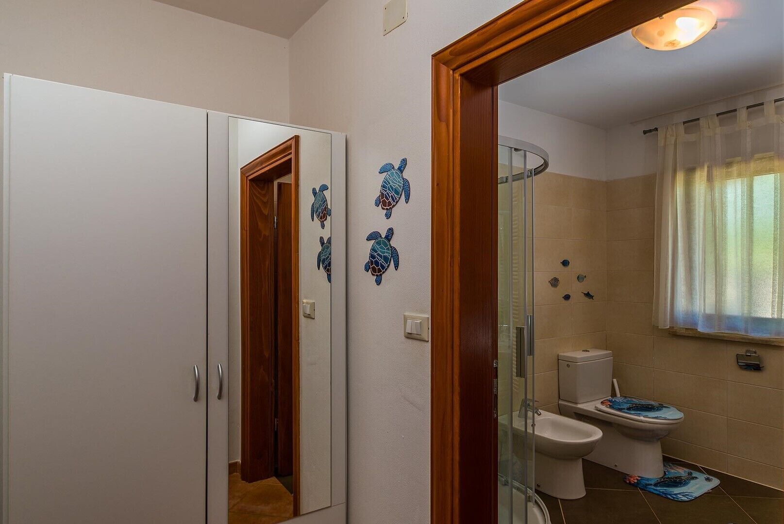 Un bagno con box doccia in vetro, un water decorato con una tartaruga marina blu e uno specchio con cornice in legno.