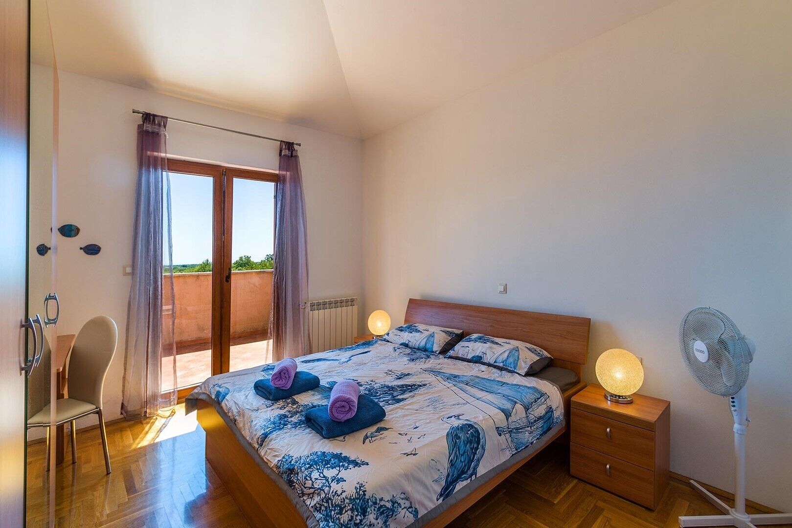 Une chambre à coucher avec un lit, des lampes de chevet, une chaise et un ventilateur.