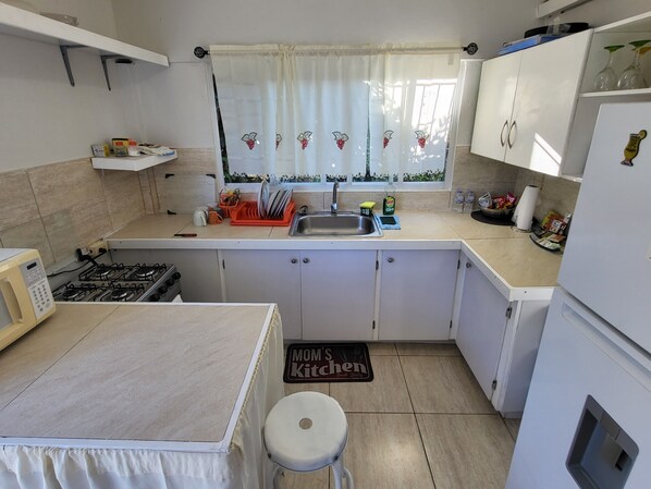 Une cuisine équipée d’une cuisinière à gaz, d’un évier et d’une fenêtre avec un rideau.
