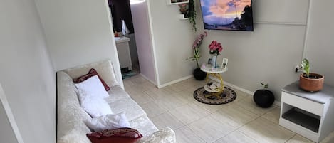 A living room with a sofa, a television mounted on the wall, a small table with a vase, and a potted plant.