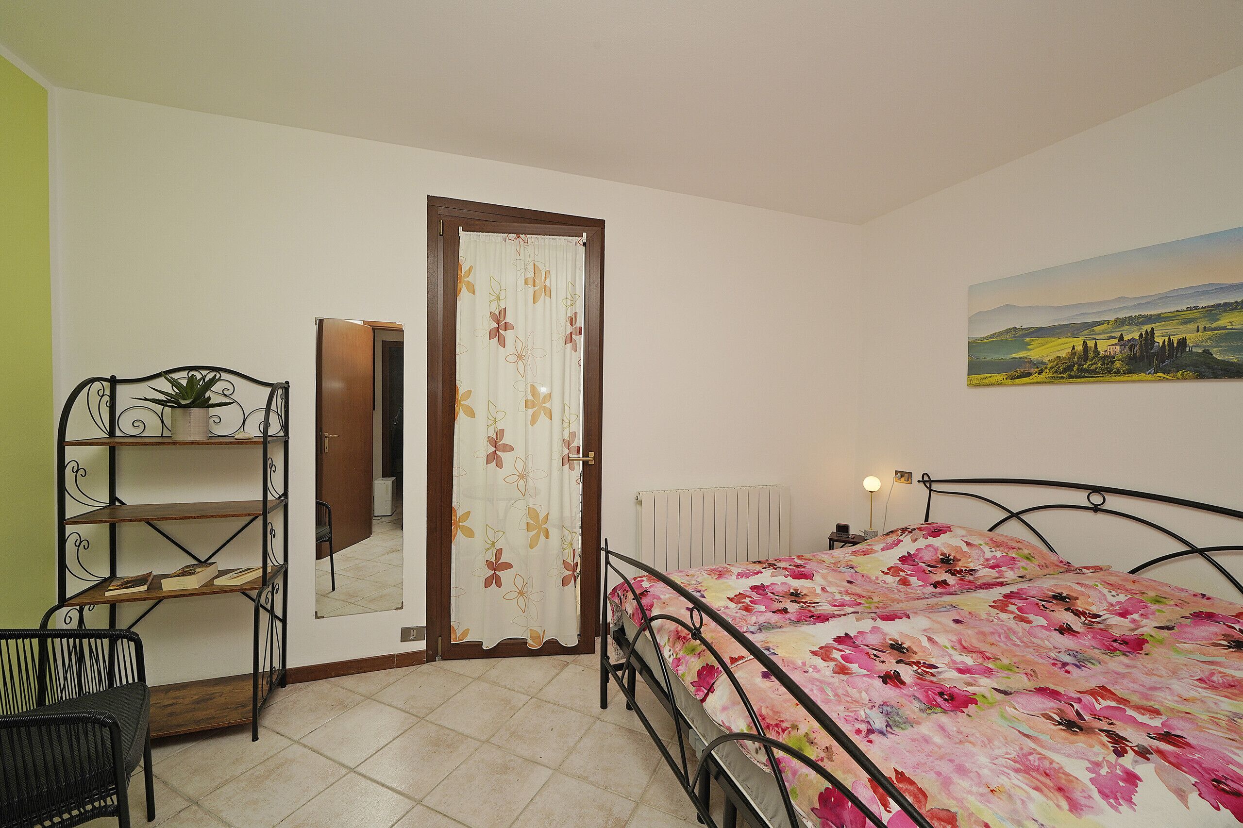 Una camera da letto con un letto, una sedia, uno scaffale con una pianta, una porta e un quadro appeso al muro.