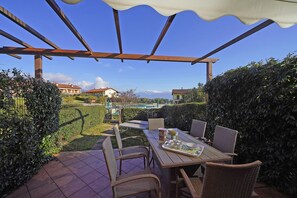 A patio with a table set for four, surrounded by wicker chairs, overlooking a pool and mountains. - Appartamento Borgo Alto (Puegnago del Garda)