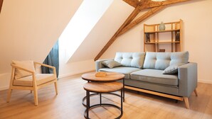 Et loftrum med træloft, en grå sofa, en træstol og et lille rundt bord.