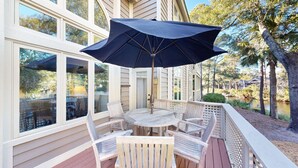 Un espacio de estar techado al aire libre con una mesa y sillas, con vistas a un cuerpo de agua y árboles.