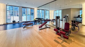 Ett modernt gym med stora fönster, trägolv och olika typer av träningsutrustning.