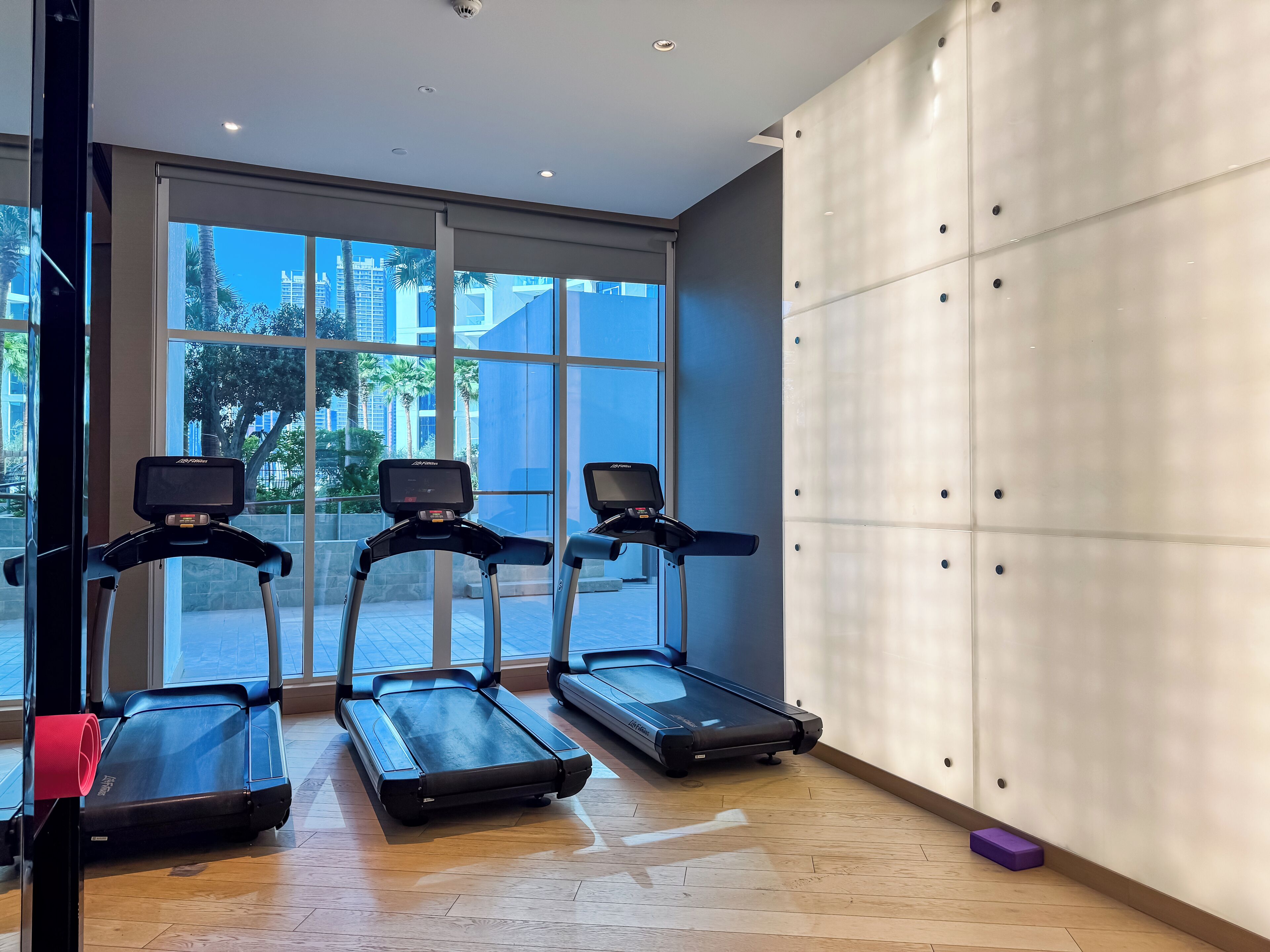 A gym with three treadmills, large windows, and a wooden floor.