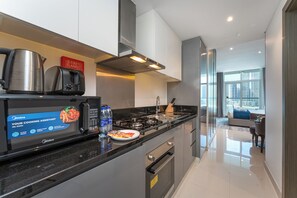 A modern kitchen with a built-in microwave, a kettle, and a toaster. There is a sign for a fire blanket, and a plate with food on the counter. - PVH - Damac Prive - Studio - Canal View (Dubai)