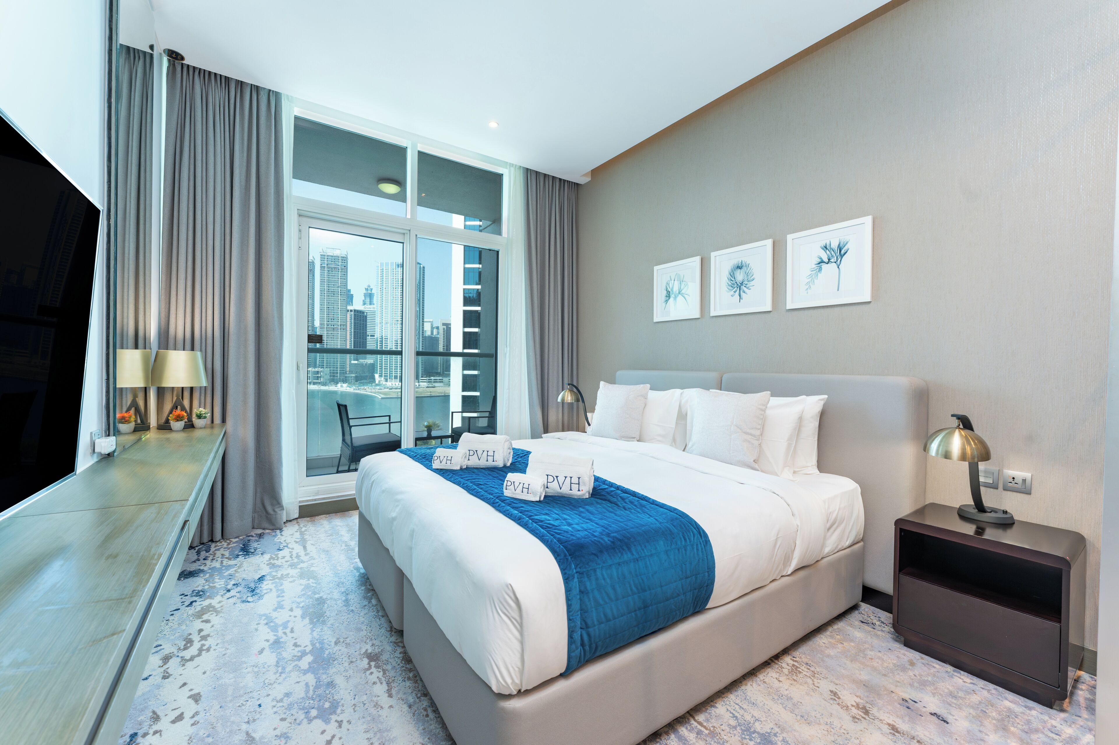 Quarto de hotel moderno com uma cama grande, televisão, escrivaninha e varanda com vista para a cidade.