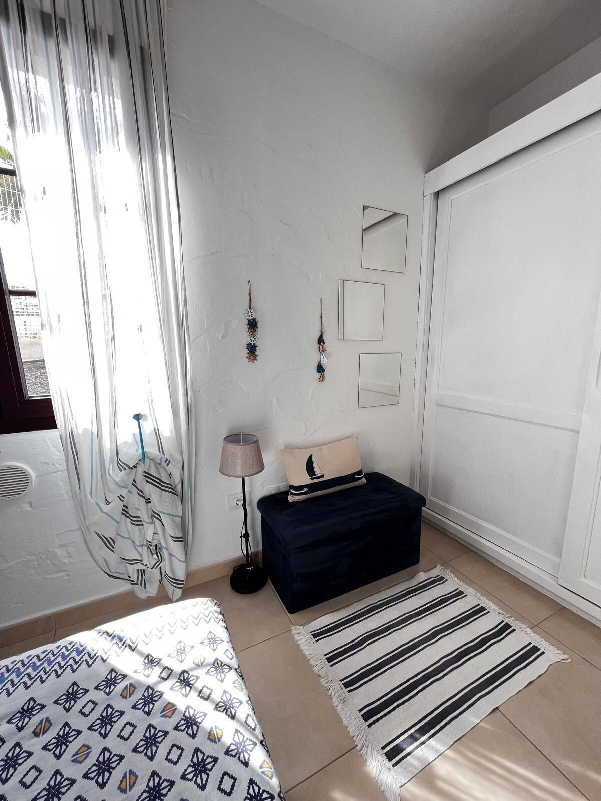 Une chambre à coucher avec un lit, une table de chevet, une lampe, une commode et une fenêtre avec des rideaux.