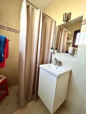 A bathroom with a shower curtain, a sink with a mirror, and a red stool. - La Casita Sun Beach (Castillo Caleta de Fuste)