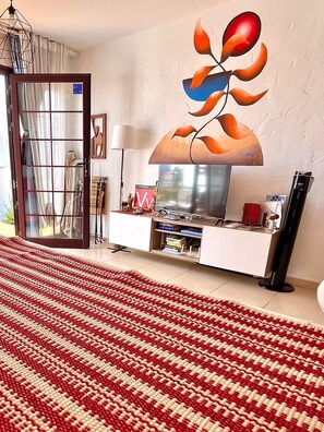 A living room with a large TV, a red and white striped rug, and a wall art piece. - La Casita Sun Beach (Castillo Caleta de Fuste)