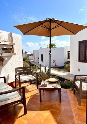 A patio with a table, chairs, and an umbrella. There are plants and a small garden area. - La Casita Sun Beach (Castillo Caleta de Fuste)