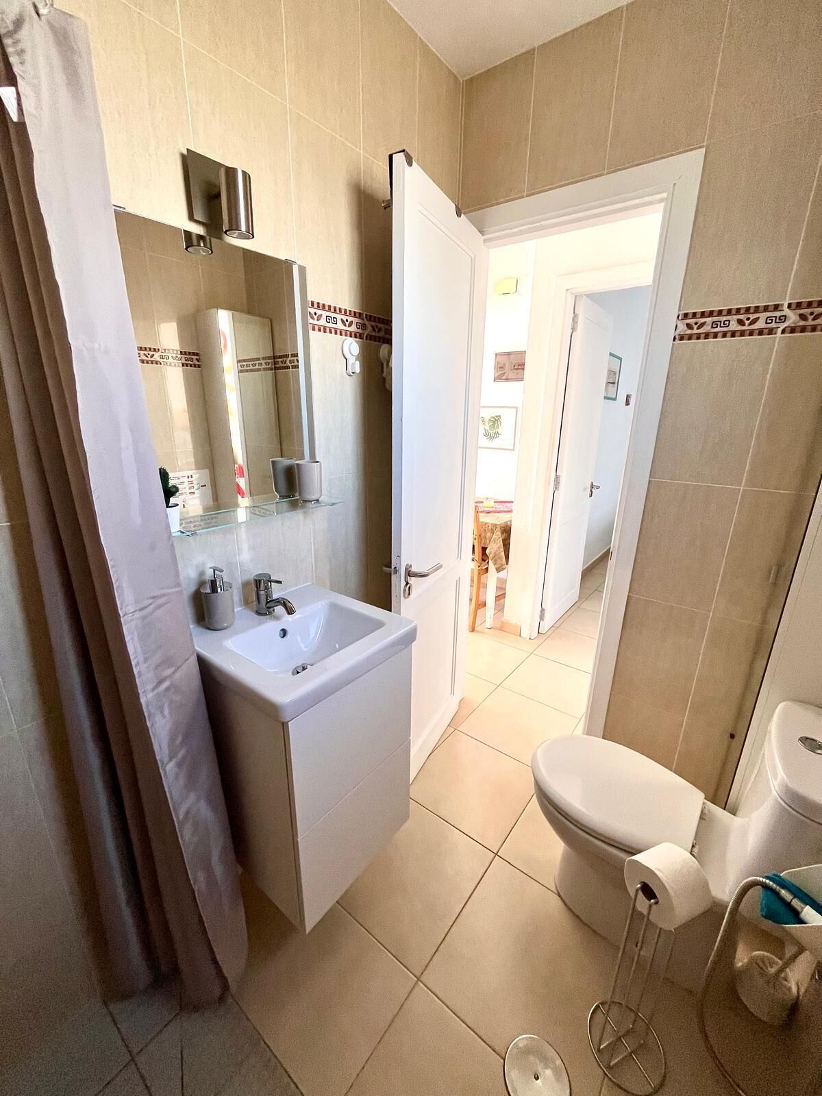 Une salle de bain équipée d’un lavabo, d’un miroir, de toilettes et d’un rideau de douche.