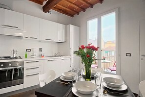Une cuisine moderne avec des meubles blancs, une table à manger dressée pour quatre personnes et une vue sur l’extérieur.