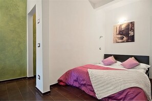 Une chambre à coucher avec un lit, des oreillers, une œuvre d’art accrochée au mur et une porte.