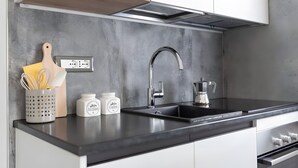 Una cocina moderna con encimera negra, pileta de acero inoxidable y armarios blancos.