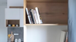 Una estantería con libros y una zona de cocina con tabla de cortar, cuchillo y recipientes.