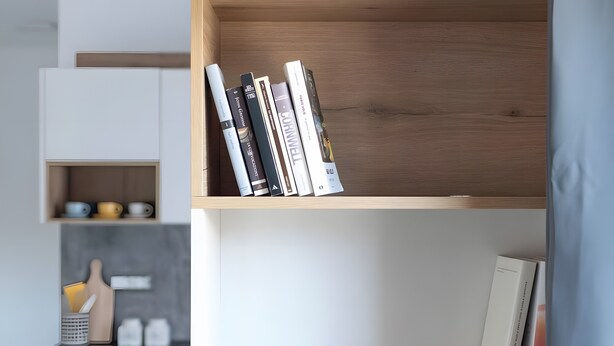 Una estantería con libros y una zona de cocina con tabla de cortar, cuchillo y recipientes.
