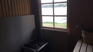 Une pièce avec une fenêtre donnant sur un plan d’eau, un banc en bois et un récipient en métal contenant du charbon de bois.